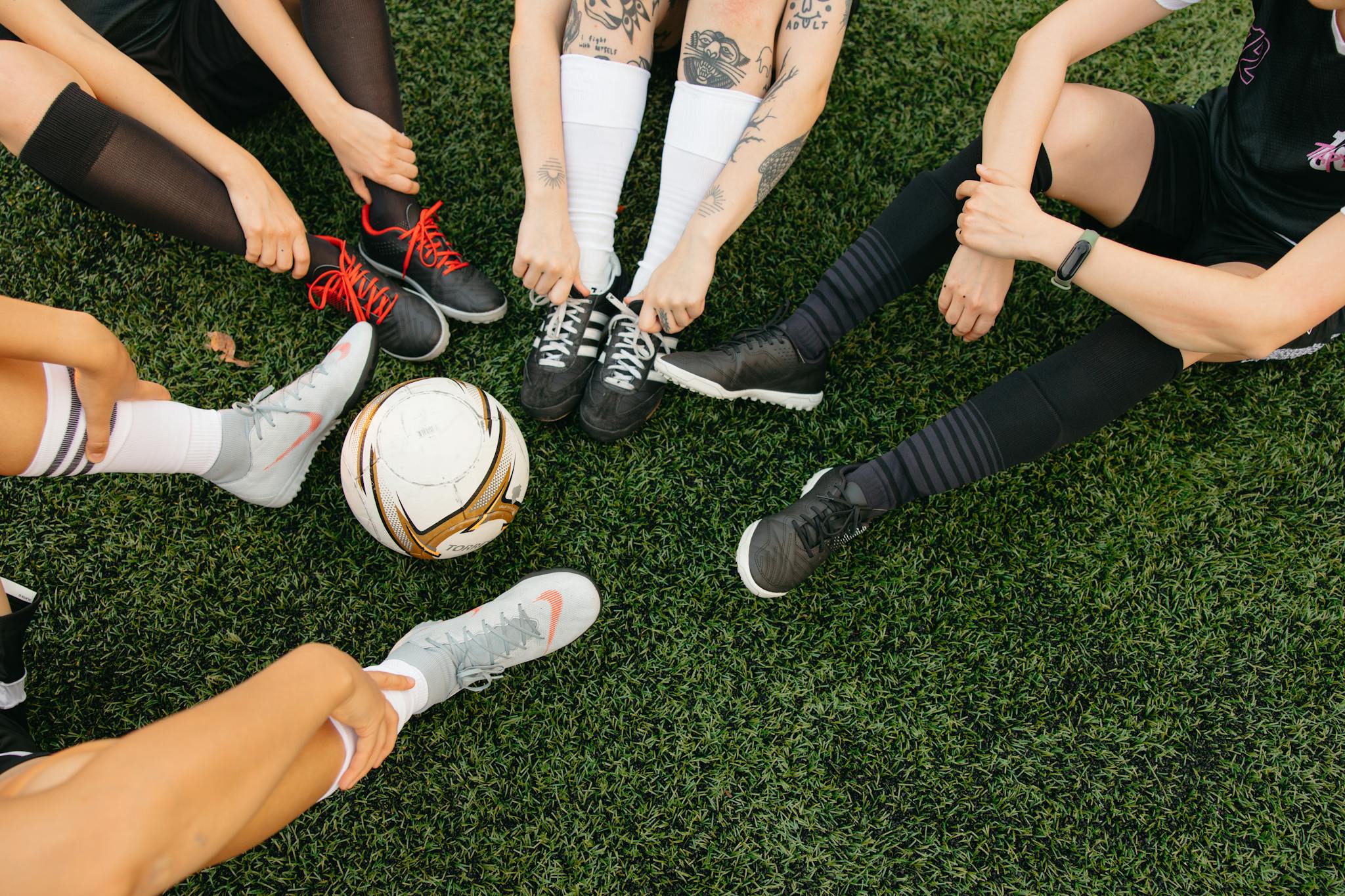 Top view of soccer players tying shoelaces on grassy field before match.