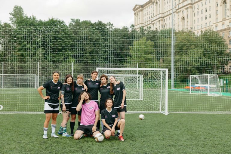 A group of women soccer players posing happily on a field, showcasing teamwork and diversity.