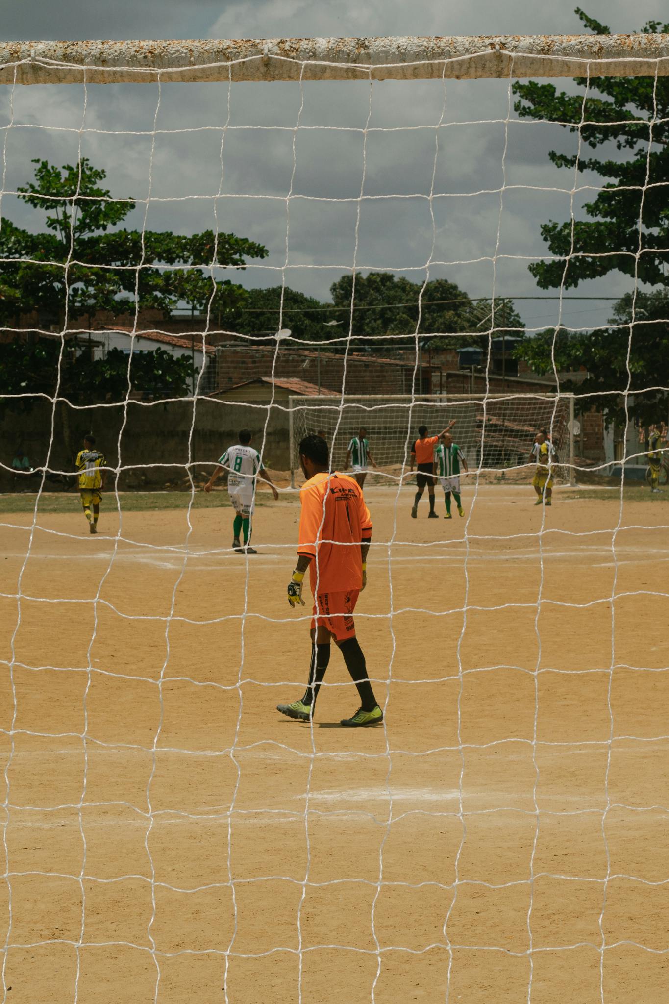 Outdoor soccer game on a sandy field in Paudalho, Brazil featuring local players.